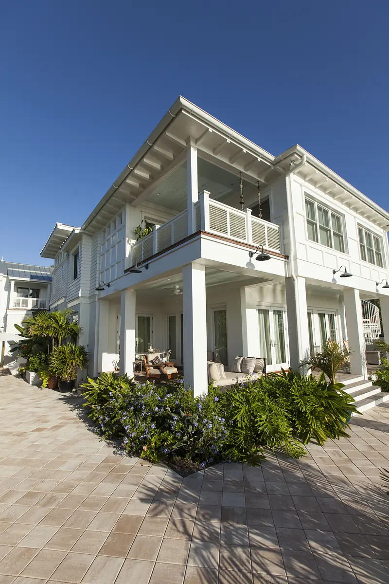 Exterior front view of a two-story house with a wraparound porch, seating, and landscaped plants.