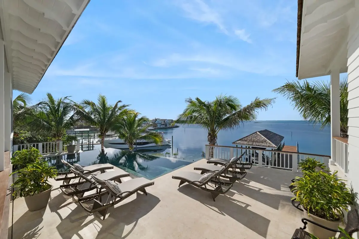 Deck with lounge chairs, infinity pool, tropical plants, and a gazebo overlooking a body of water.