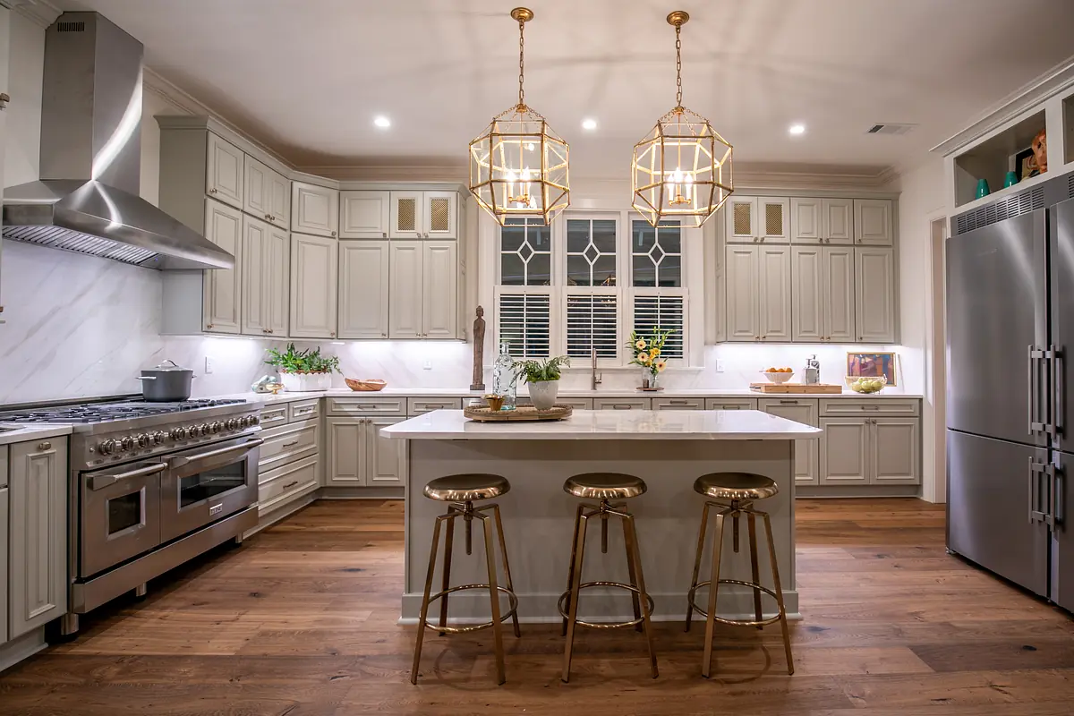 Kitchen with gray cabinetry, marble island, gold bar stools, stainless steel appliances, and wooden floor.