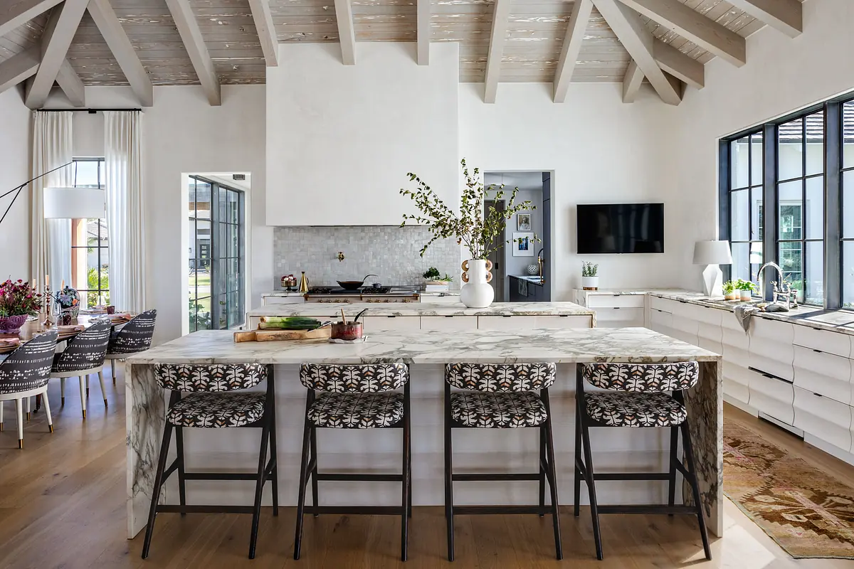 Kitchen with marble island, bar stools, white cabinetry, tiled backsplash, and stainless-steel appliances