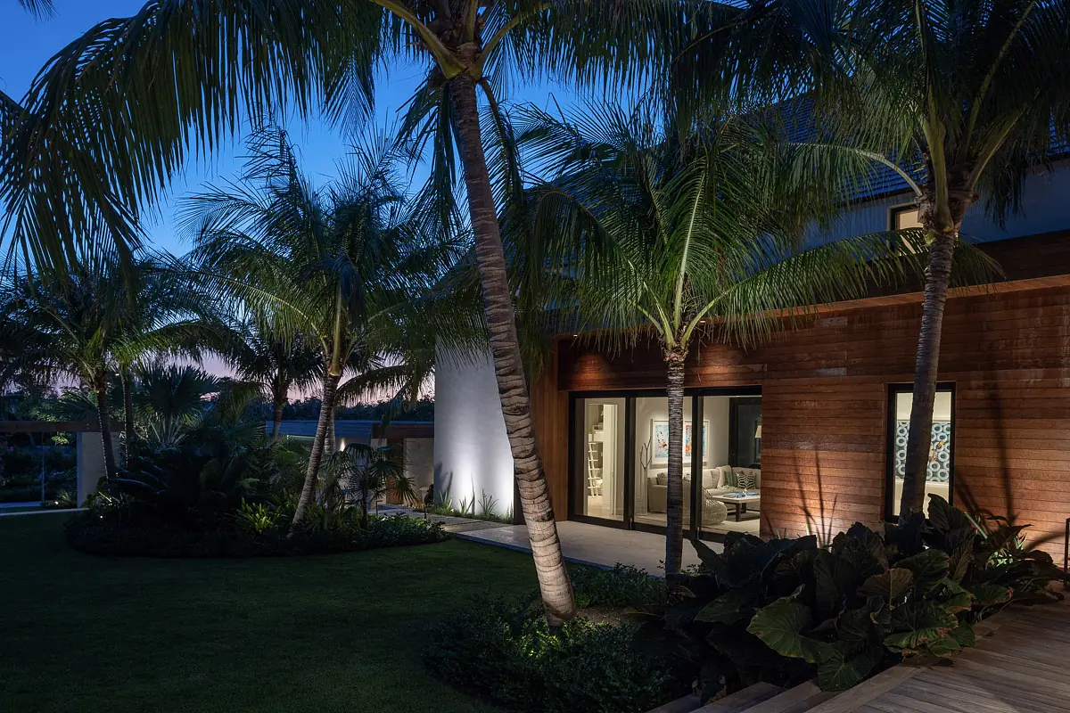 Exterior rear view with glass doors, wood paneling, palm trees, and landscaped garden at dusk.