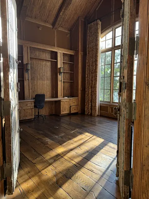 Office with wooden flooring, built-in cabinetry, desk, chair, and large windows with curtains.