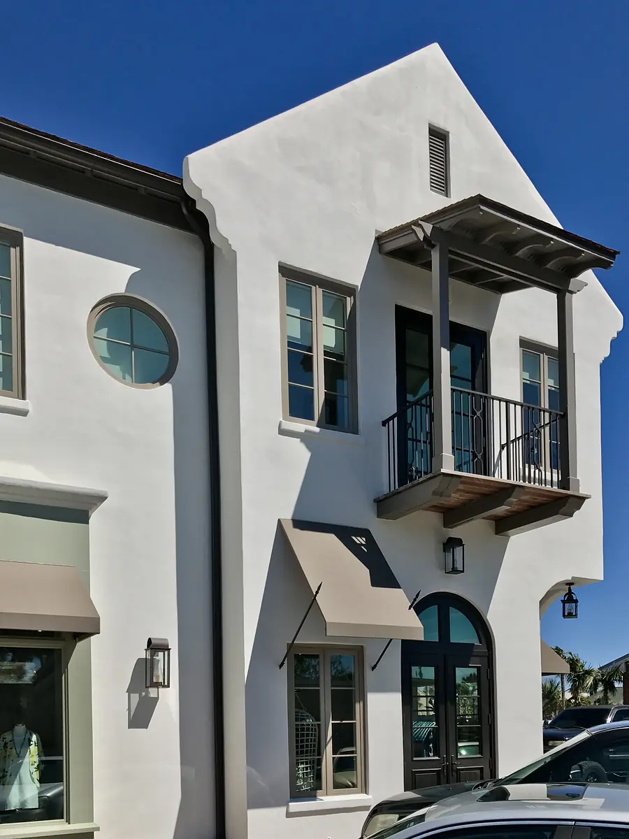 Exterior view of a building with white stucco, circular windows, balcony, and decorative lanterns.