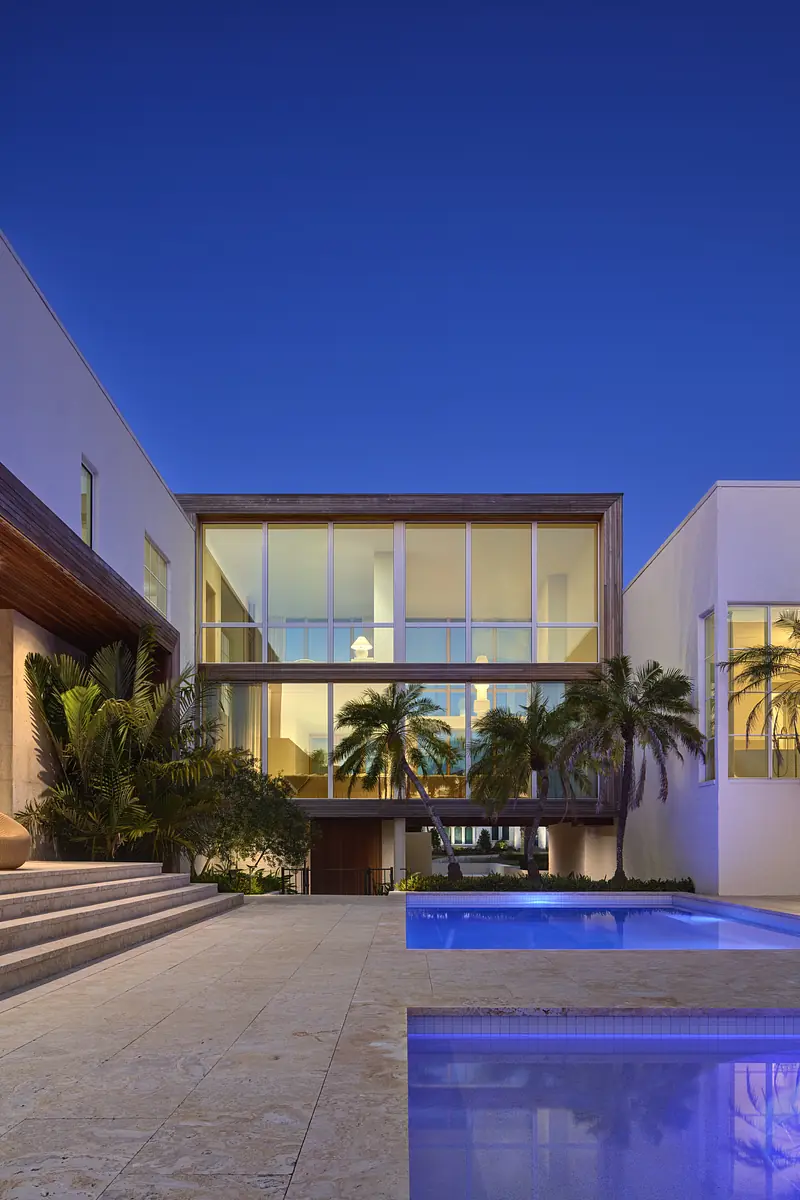 Exterior view of a house with glass wall, wooden accents, palm trees, and a swimming pool