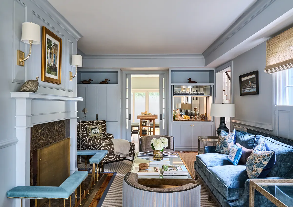 Living room with blue velvet sofa, glass coffee table, patterned armchair, built-in shelves, and stone fireplace.