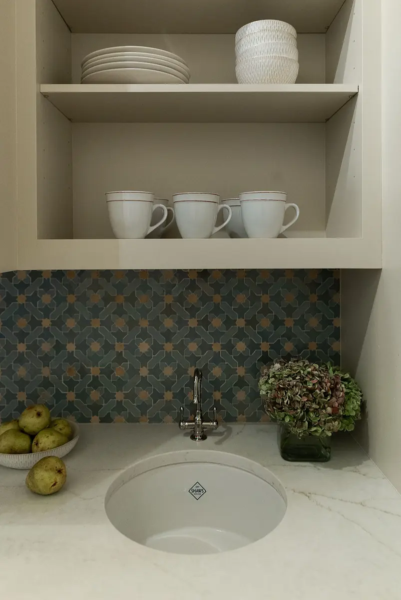 Butler's pantry with sink, countertop, ceramic cups, plates, bowl of pears, and decorative vase.