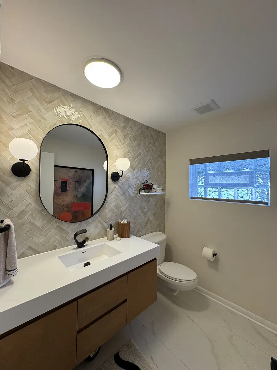 Bathroom with floating vanity, double basin sink, round mirror, beige herringbone tile, and natural light.
