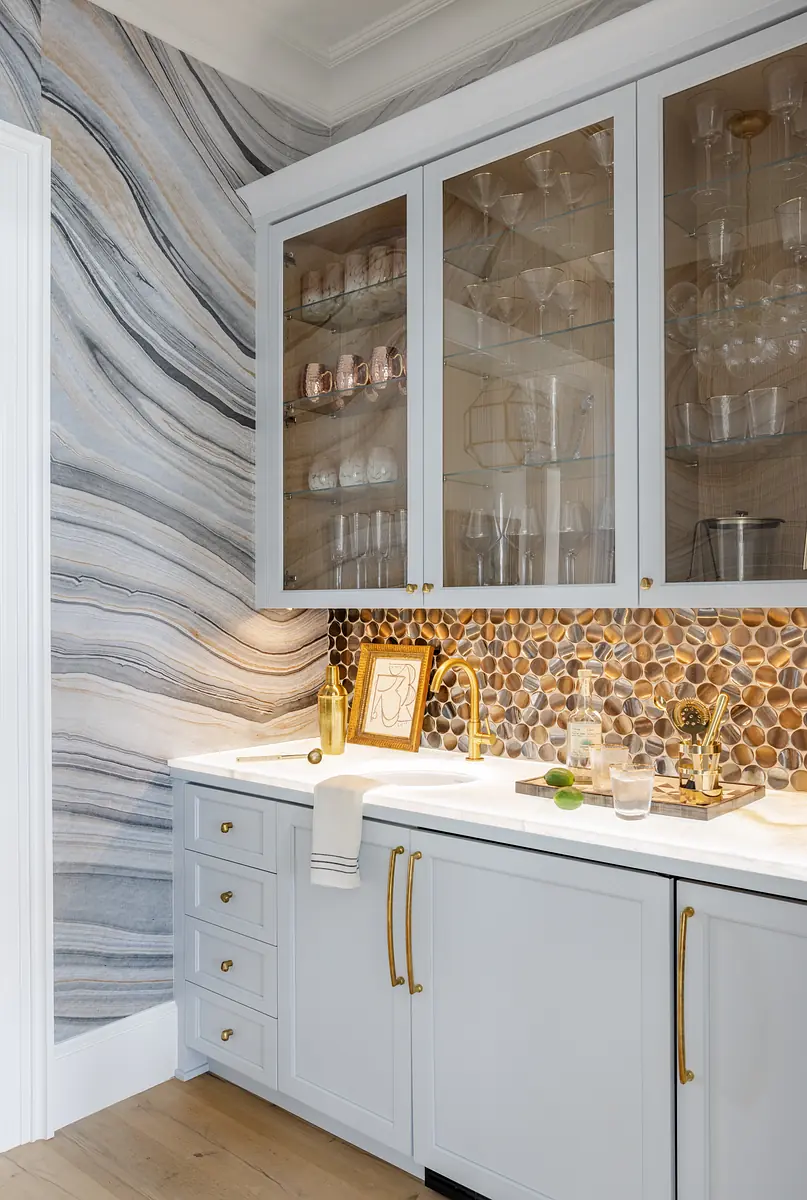 Kitchen with light blue cabinets, white countertop, stone backsplash, gold faucet, and marble wall.