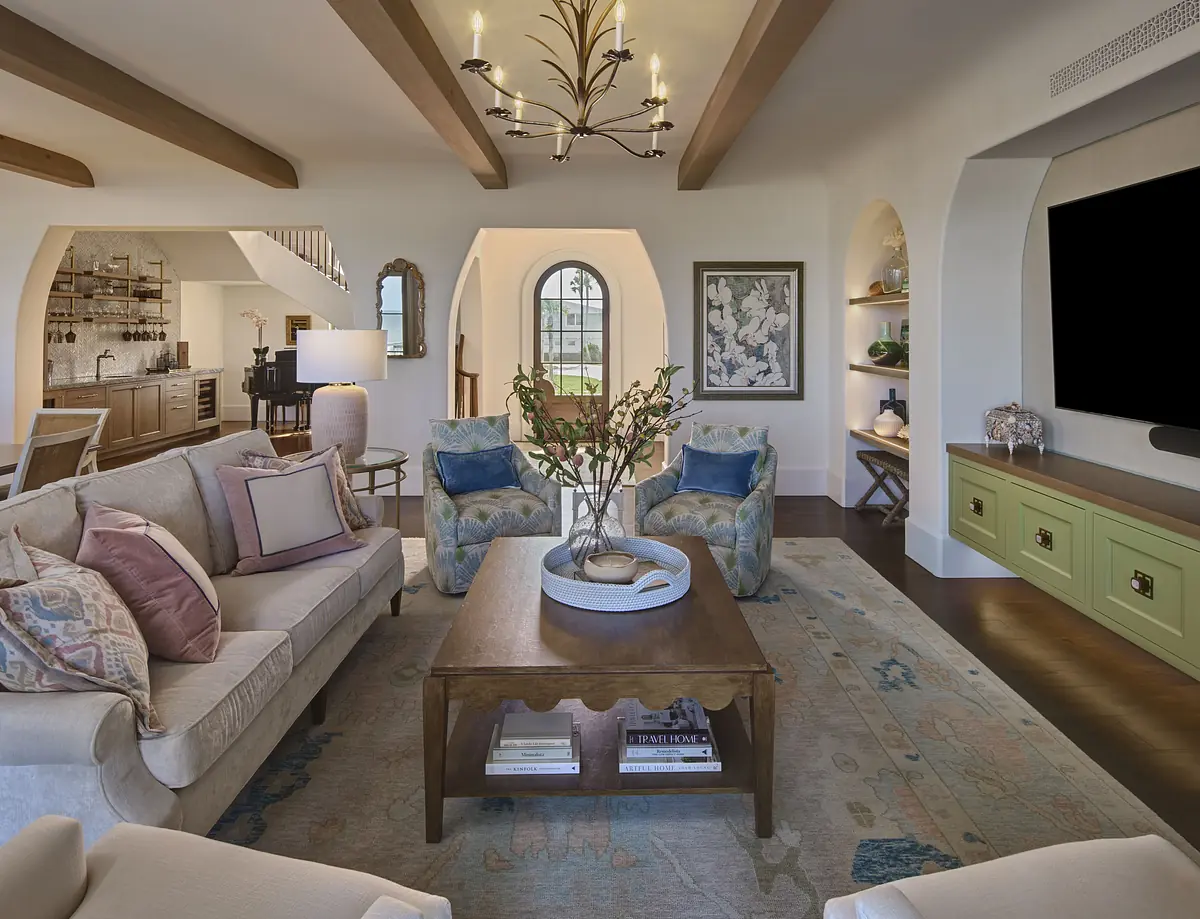 Living room with light-colored sofa, armchairs, wooden coffee table, large television, and decorative elements.
