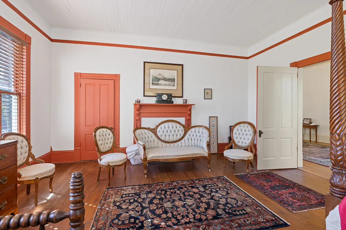 Living room with vintage sofa, upholstered chairs, decorative rugs, and wooden floors with orange trim.