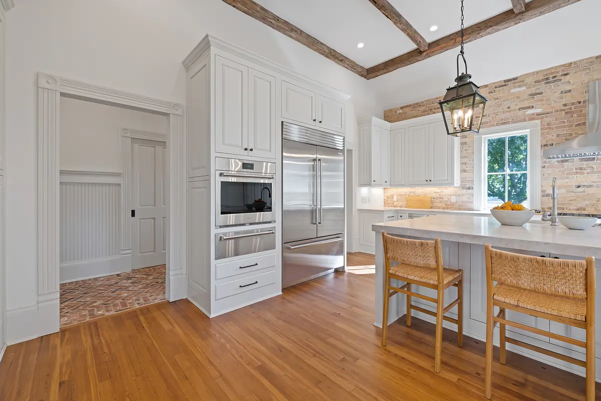 Kitchen with white cabinetry, stainless steel appliances, island with seating, and brick accent wall.