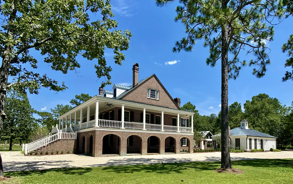 Two-story brick house with large front porch, gravel driveway, and green lawn.