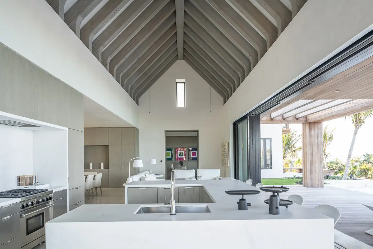 Kitchen with white island, gray cabinetry, stainless steel appliances, high ceilings, and a glass wall opening to outdoors.