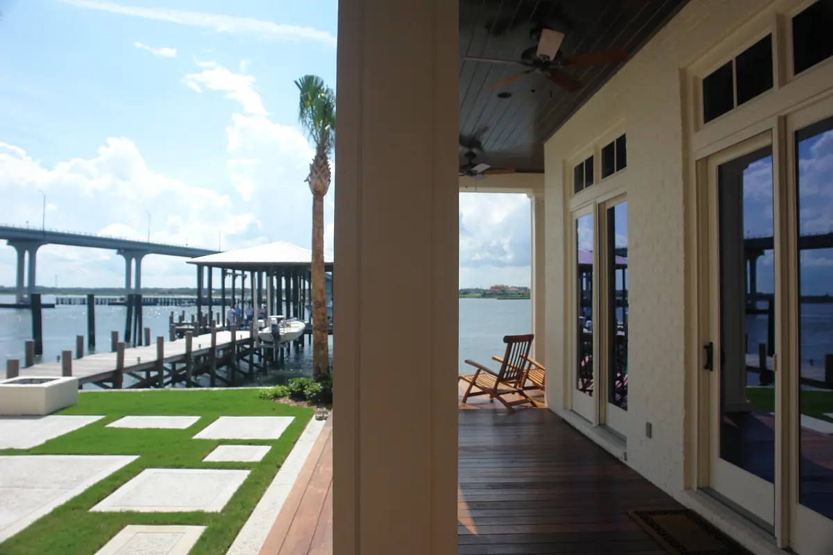 Patio with rocking chair, concrete pavers, grass, and view of water and dock.