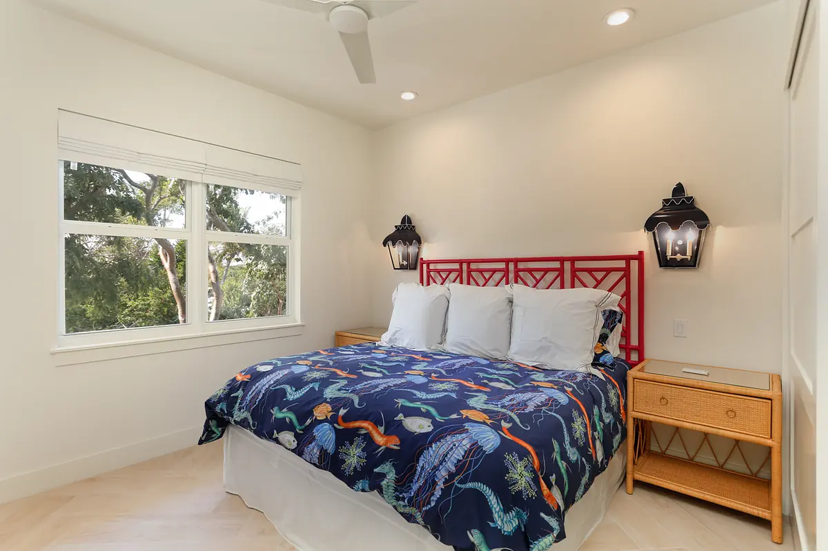 Bedroom with bed, blue quilt, nightstands, wall sconces, and windows