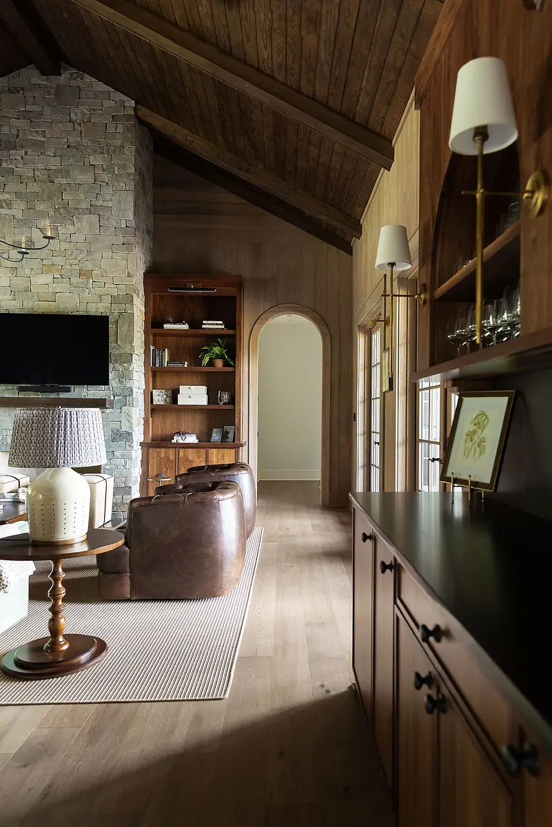 Living room with stone wall, wooden ceiling, leather armchairs, side table, and dark wood cabinet.
