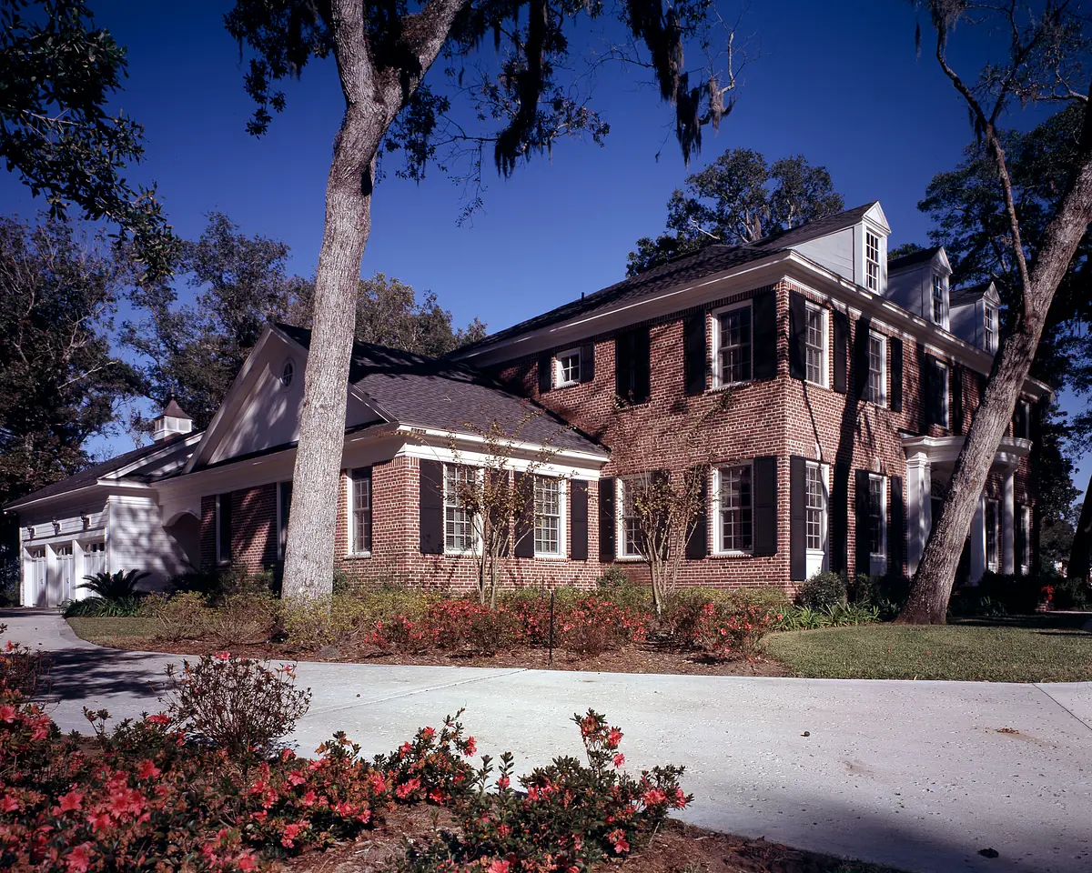 Exterior front view of a brick house with black shutters, driveway, and landscaped gardens.