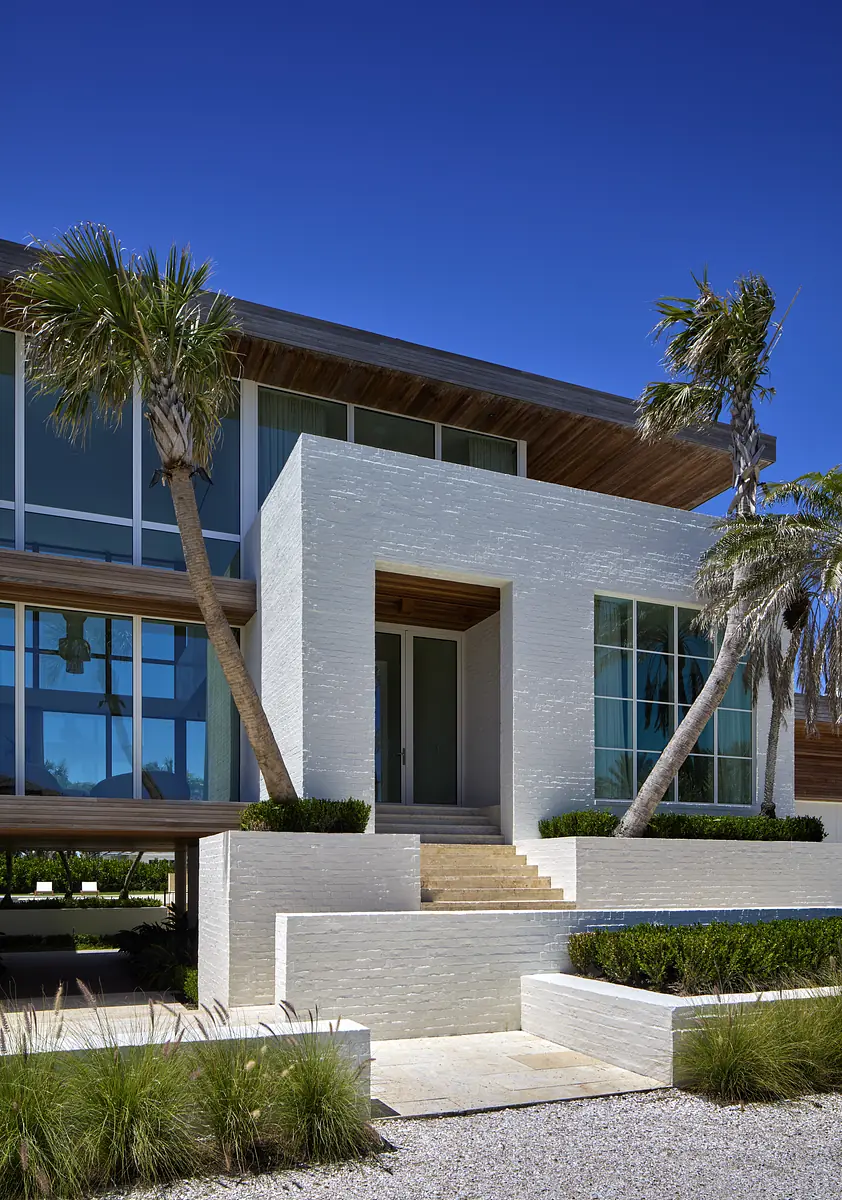 Exterior front with textured facade, large glass windows, palm trees, and landscaped entrance steps.