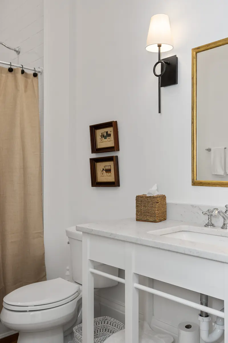 Bathroom with white vanity, marble countertop, beige shower curtain, toilet, and two framed pictures.
