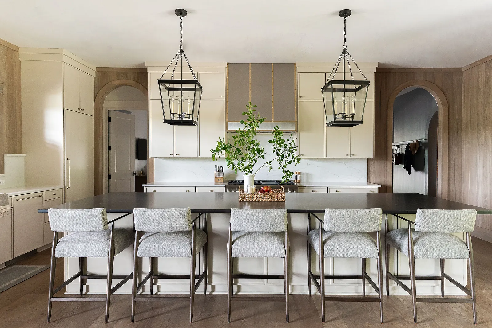 Kitchen with large island, gray stools, light wood cabinetry, marble countertop, and arched doorway