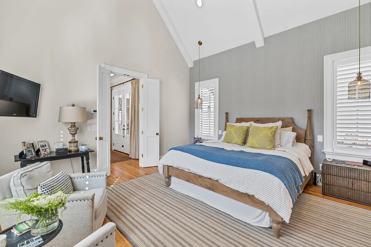 Bedroom with brown bed, white bedding, green pillows, nightstands, lamp, and light gray textured walls.