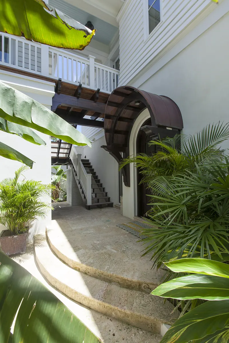 Exterior front with curved entry, metal roof, stone pathway, stairs, and tropical plants.