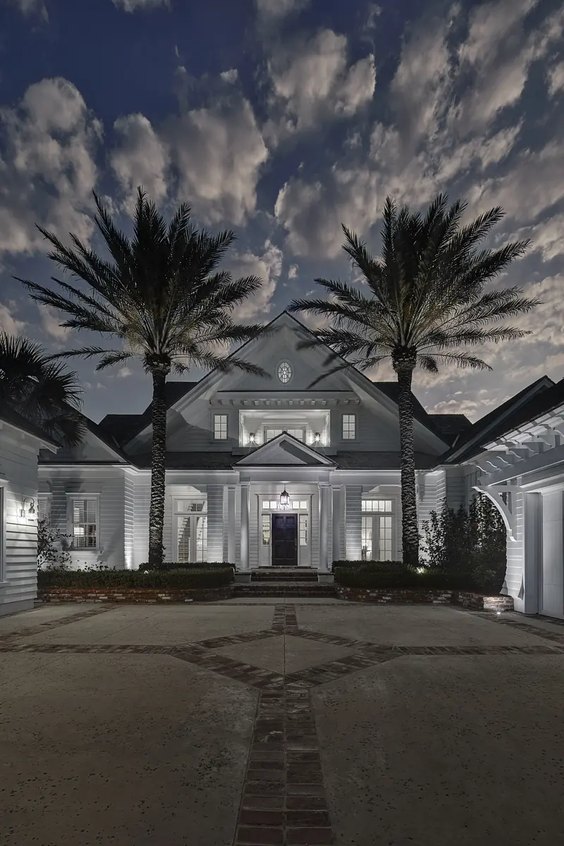Exterior front view of a house with double doors, palm trees, and a circular brick pathway.