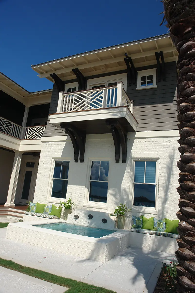 Exterior view of a two-story house with white brick, balcony, windows, and outdoor seating with a fountain.