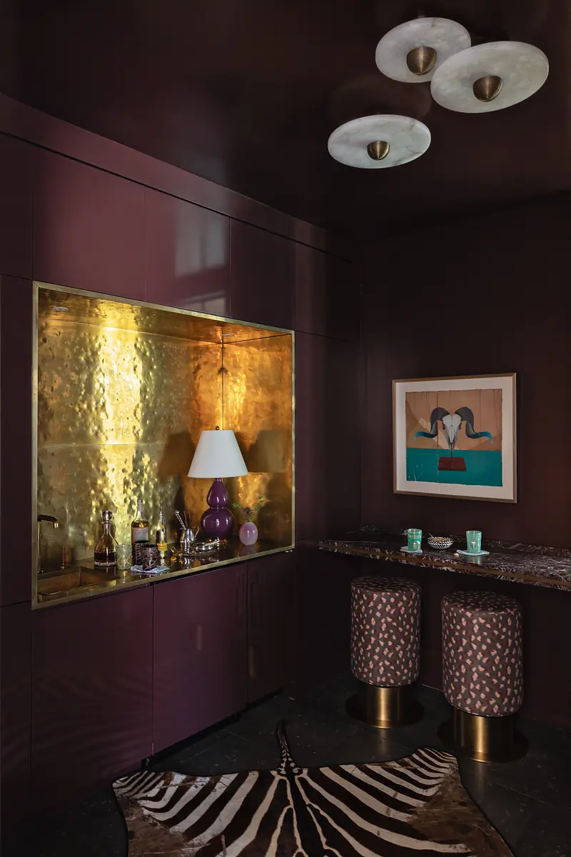Bar area with dark purple cabinetry, gold backlit feature, black stone countertop, and patterned stools