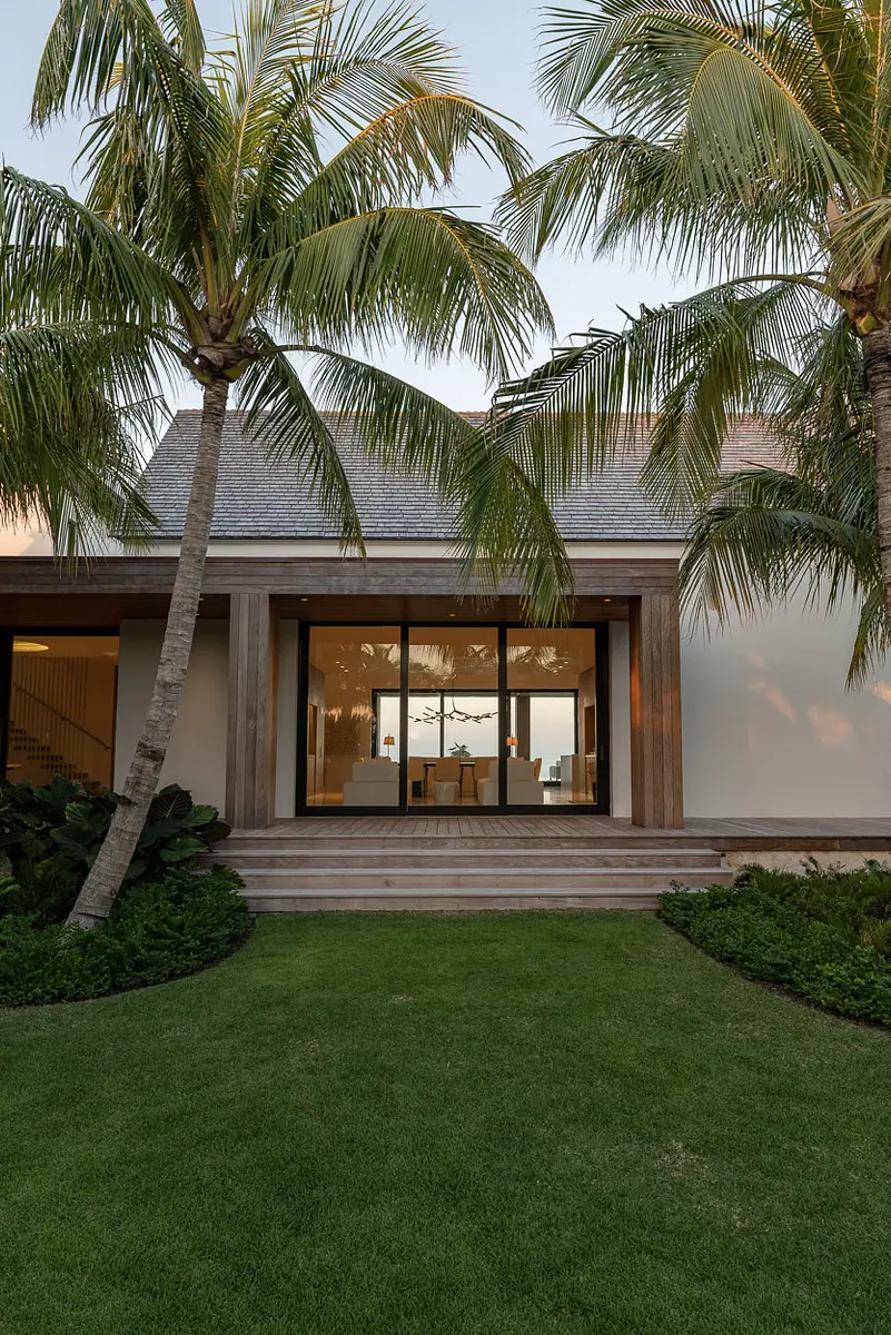 Exterior front view with large glass doors, palm trees, and well-maintained lawn and garden.