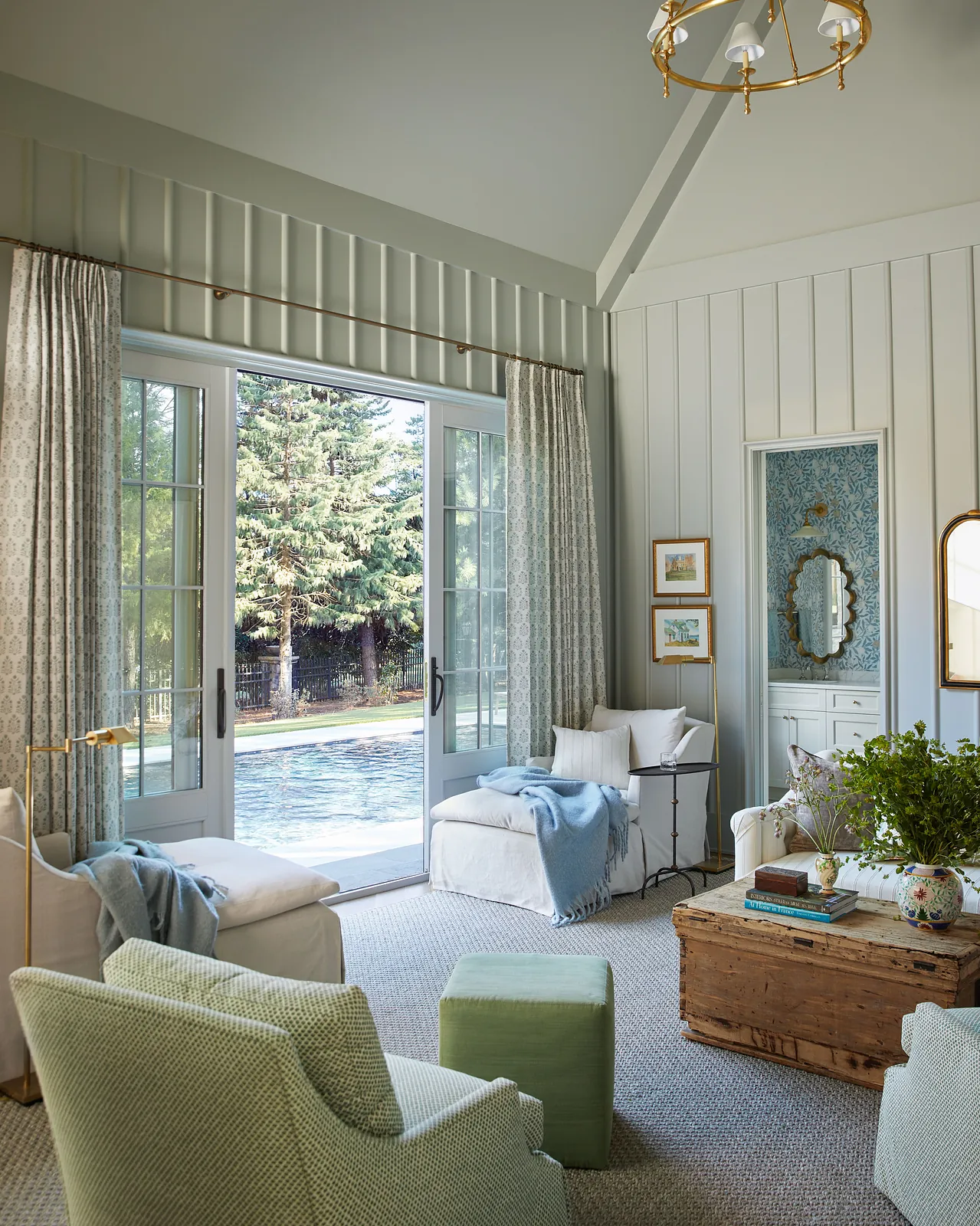 Living room with white armchairs, green ottoman, wooden coffee table, area rug, and large sliding glass doors