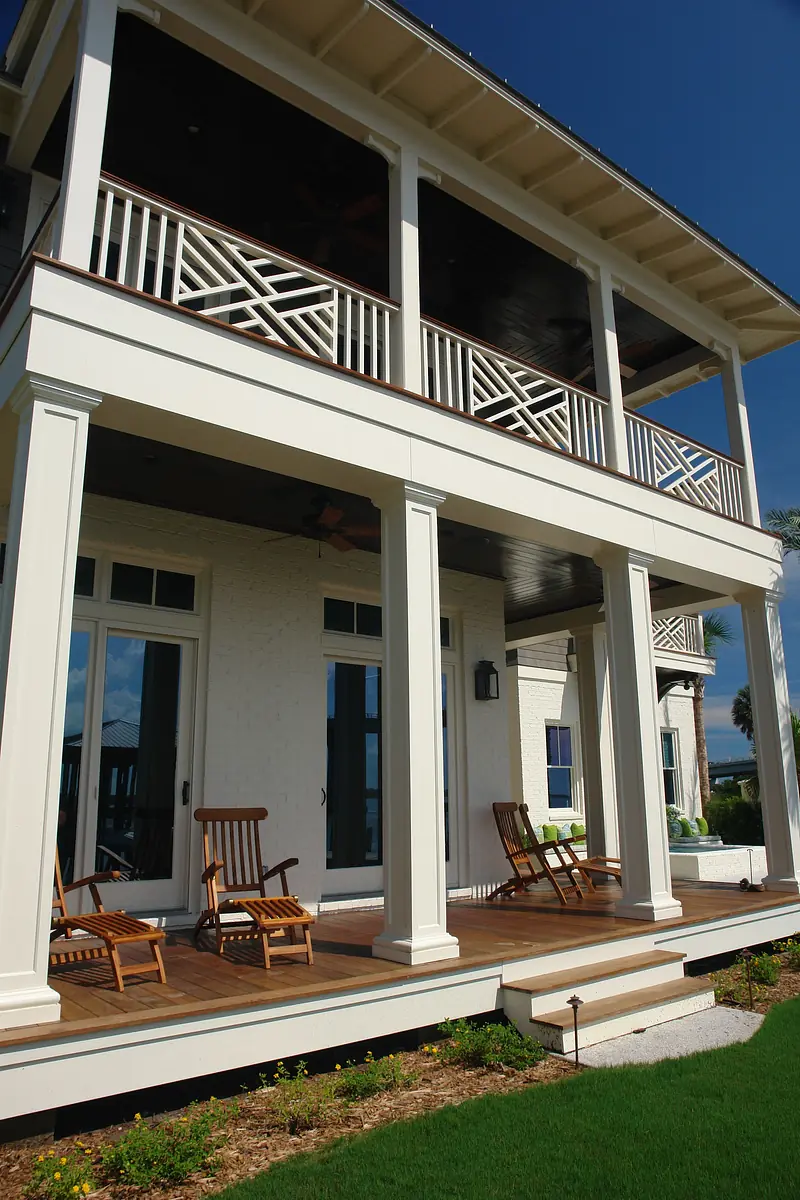 Deck with two wooden rocking chairs, wooden surface, white brick walls, and large glass doors.