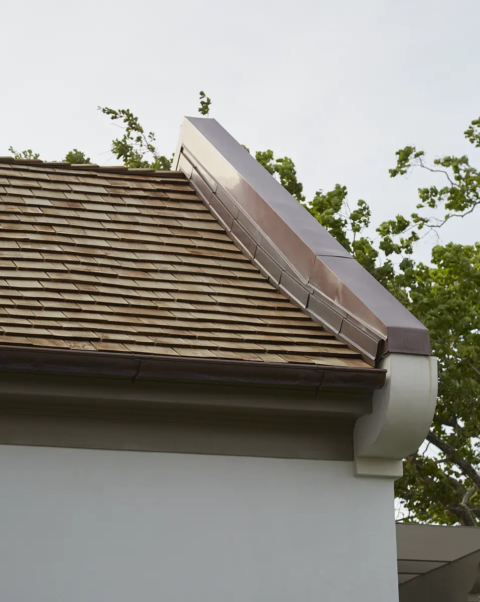Exterior front with sloped wooden shingle roof, copper flashing, and white wall, surrounded by trees.