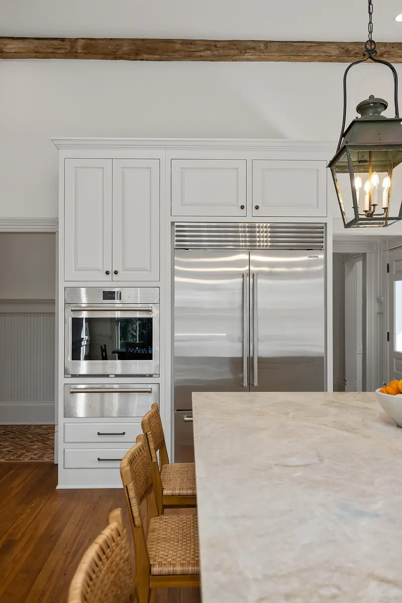 Kitchen with white cabinetry, stainless steel appliances, marble island, and woven seating.