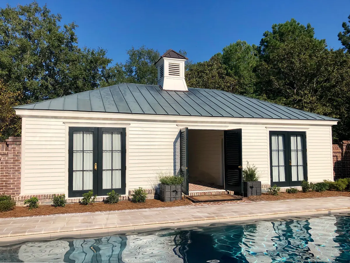 Exterior rear of a building with sloped roof, white siding, green shutters, and poolside setting.