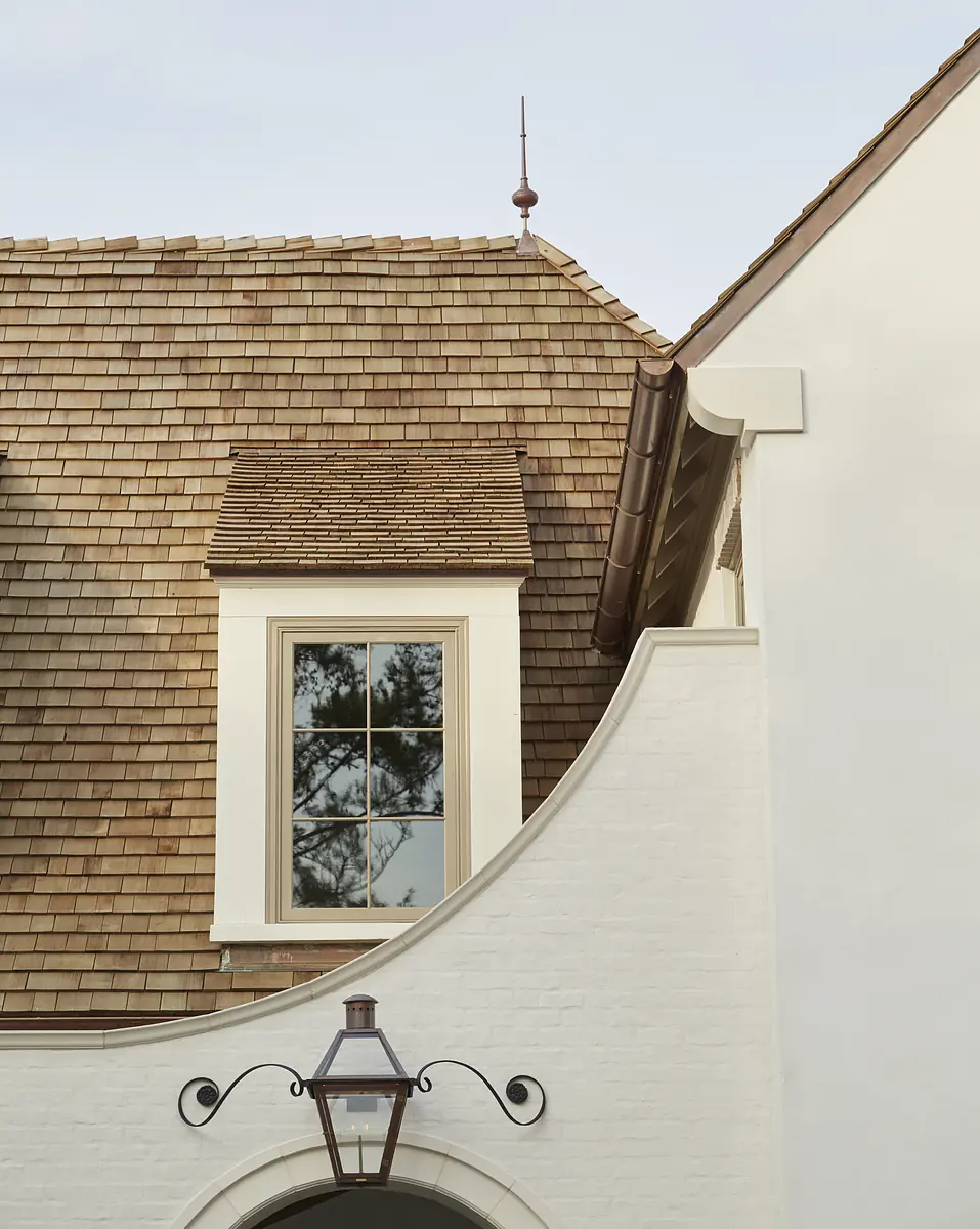Exterior front with shingled roof, window, white wall, and decorative lantern by archway.
