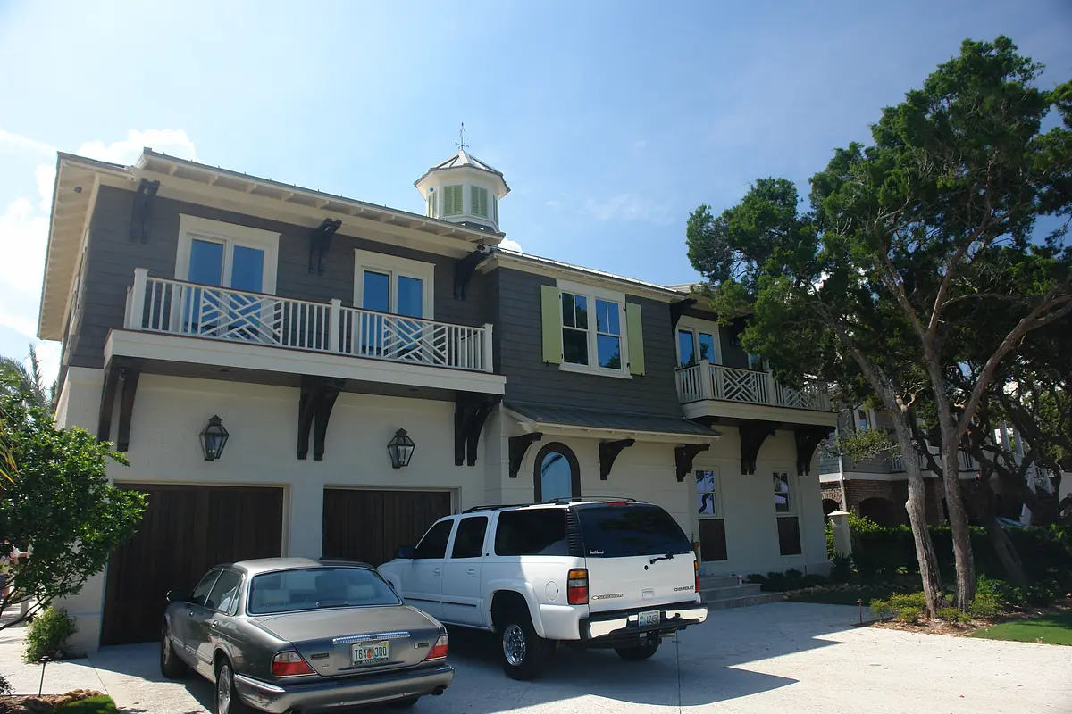 Front exterior of a two-story house with a cupola, balconies, garage doors, and landscaped driveway.