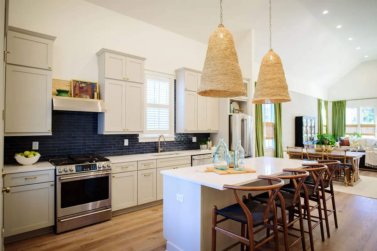 Kitchen with gray cabinetry, stainless steel oven, white island, barstools, black backsplash, and large windows.