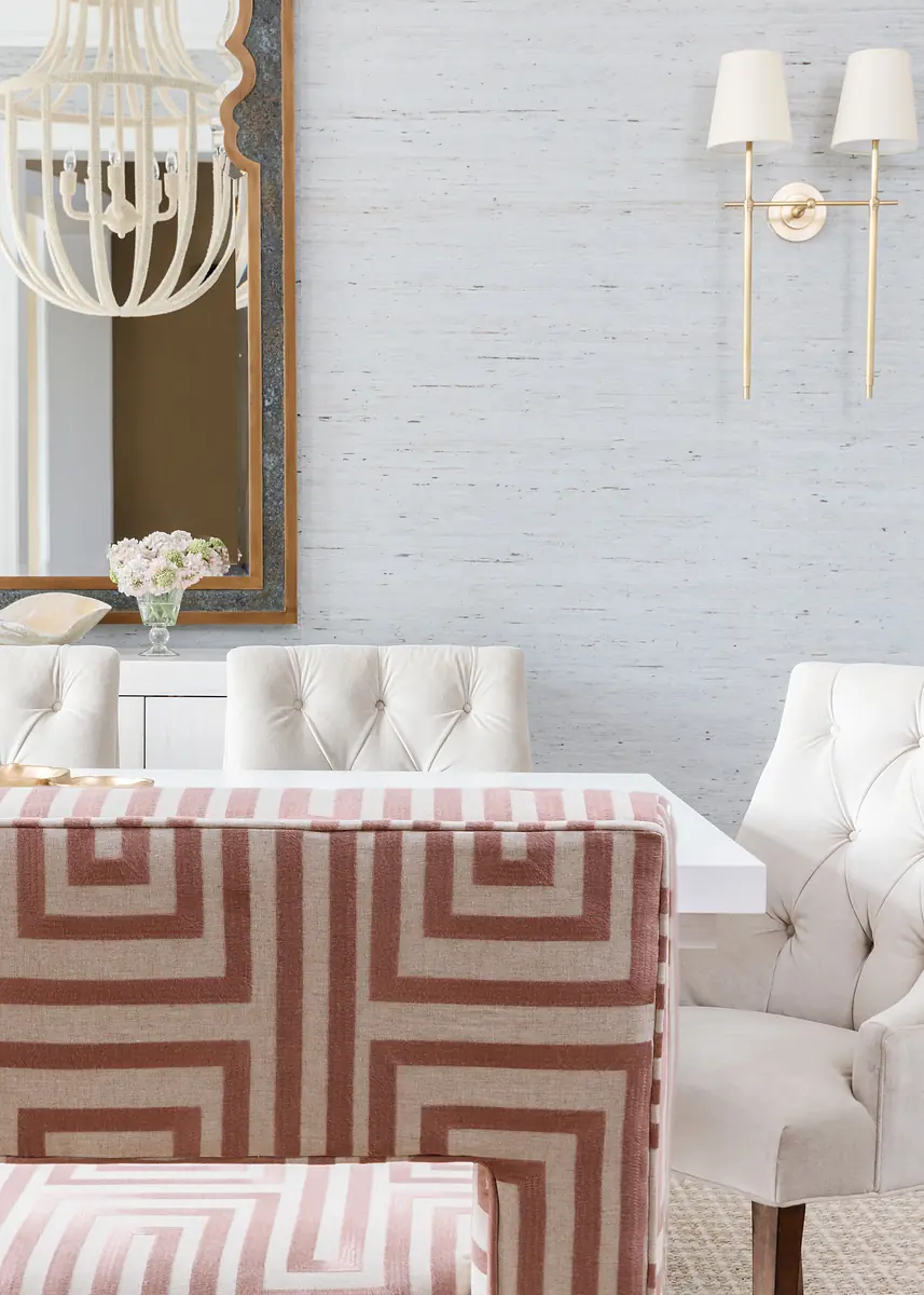 Dining room with white table, tufted chairs, pink-patterned bench, decorative mirror, and wall sconces.