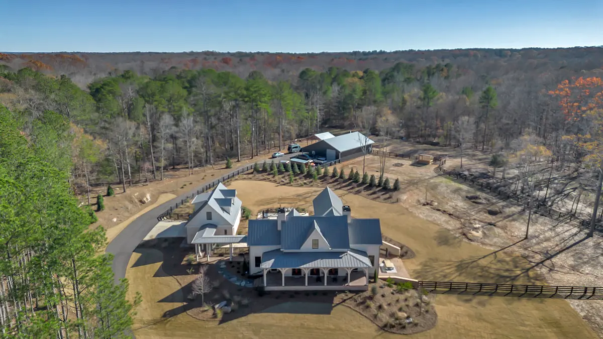 Aerial view of a property with a large house, metal roof, porches, barn, and landscaped areas.
