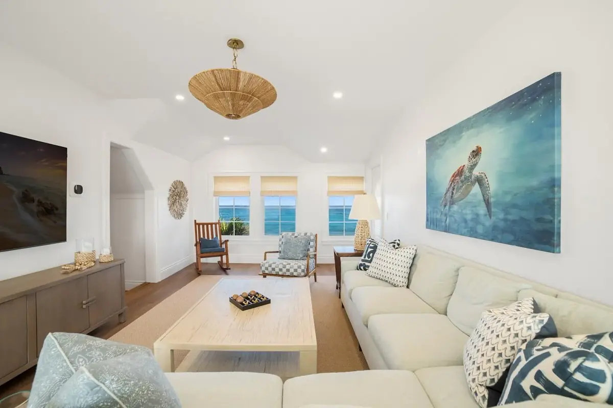 Living room with sectional sofa, coffee table, area rug, large windows, side chair, and sea turtle painting.