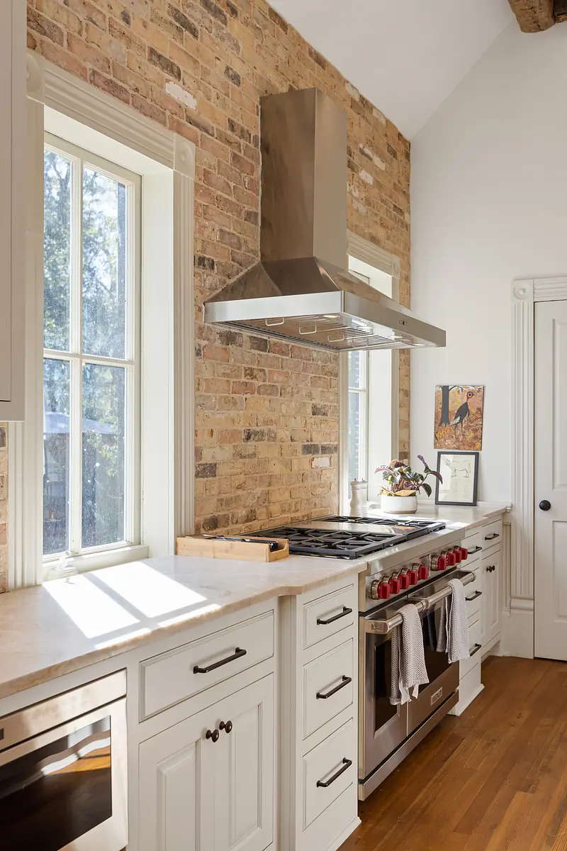 Kitchen with stainless steel stove, white cabinetry, marble countertops, and exposed brick walls.