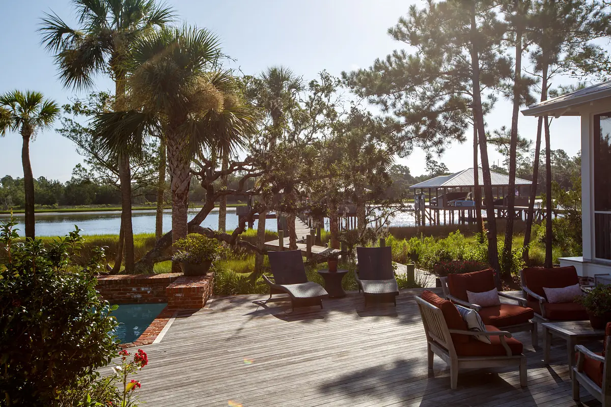 Deck with outdoor chairs, small table, greenery, and a view of water and trees in the background