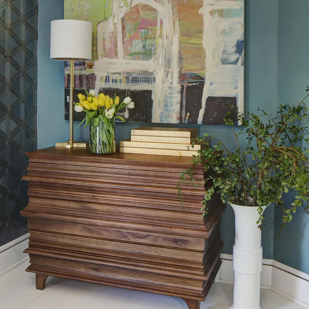 Foyer featuring a wooden console table, vases with greenery and flowers, and artwork on blue wallpapered wall.
