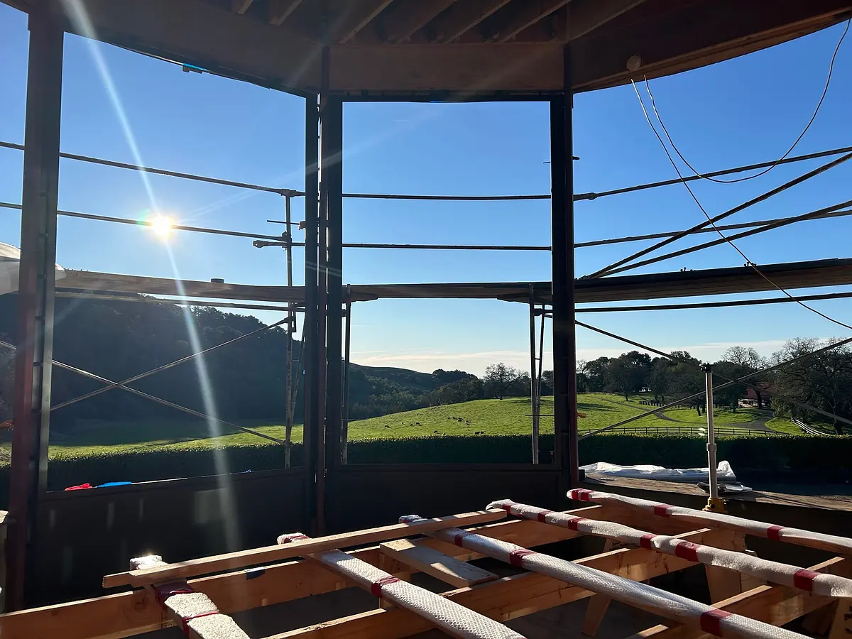 Under-construction space with wooden beams, scaffolding, and large openings for windows overlooking a landscape
