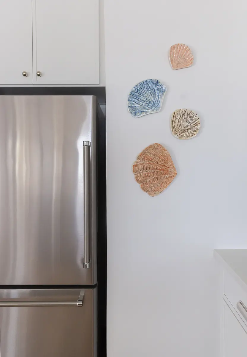 Kitchen with stainless steel refrigerator, white cabinetry, and decorative shell wall art.