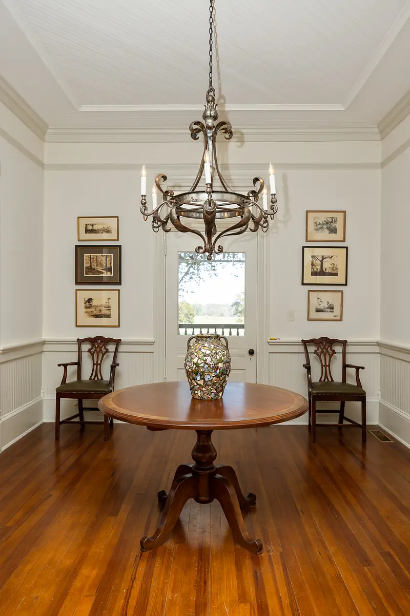 Dining room with round table, two chairs, decorative vase, framed art, and chandelier.