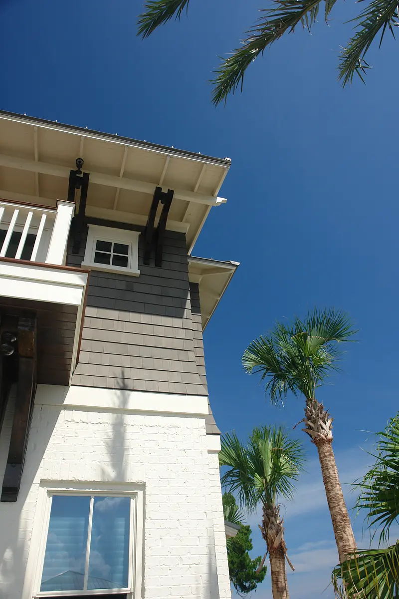 Exterior view of a two-story house with shingle siding, white brick, and palm trees.