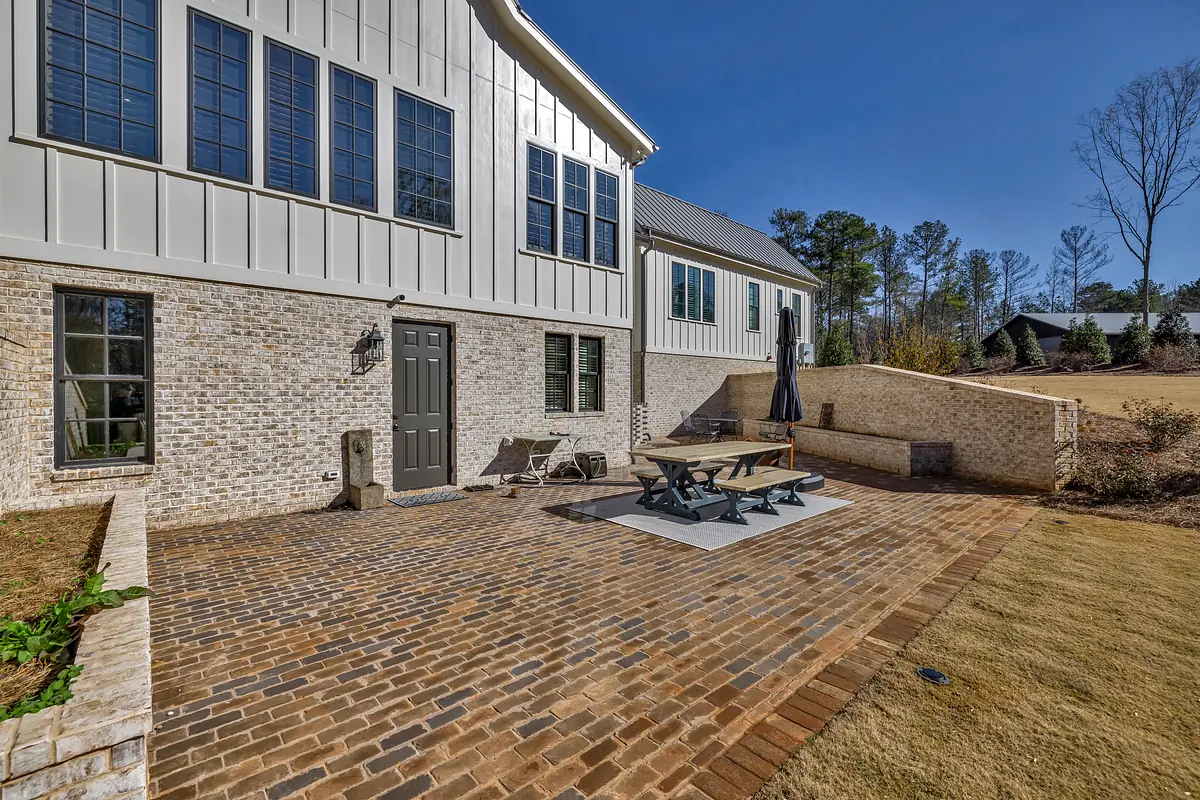 Patio with dining table, chairs, umbrella, brick pavers, and greenery along the edges.
