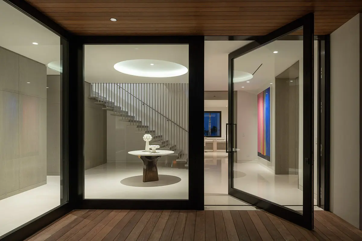 Foyer with round table, staircase, glass doors, artwork, and ceiling fixture.